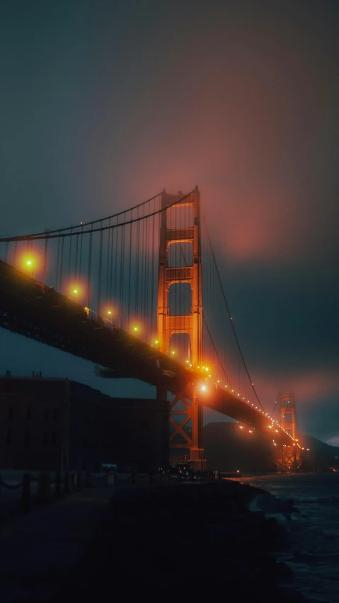 the golden gate bridge is lit up at night, by Steven James Petruccio, unsplash contest winner, hyperrealism, gothic fog ambience, retro effect, medium format color photography, yellow lights