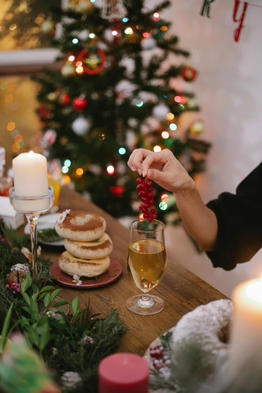 a woman sitting at a table in front of a christmas tree, food styling, breakfast, holding a glass of wine, 2019 trending photo