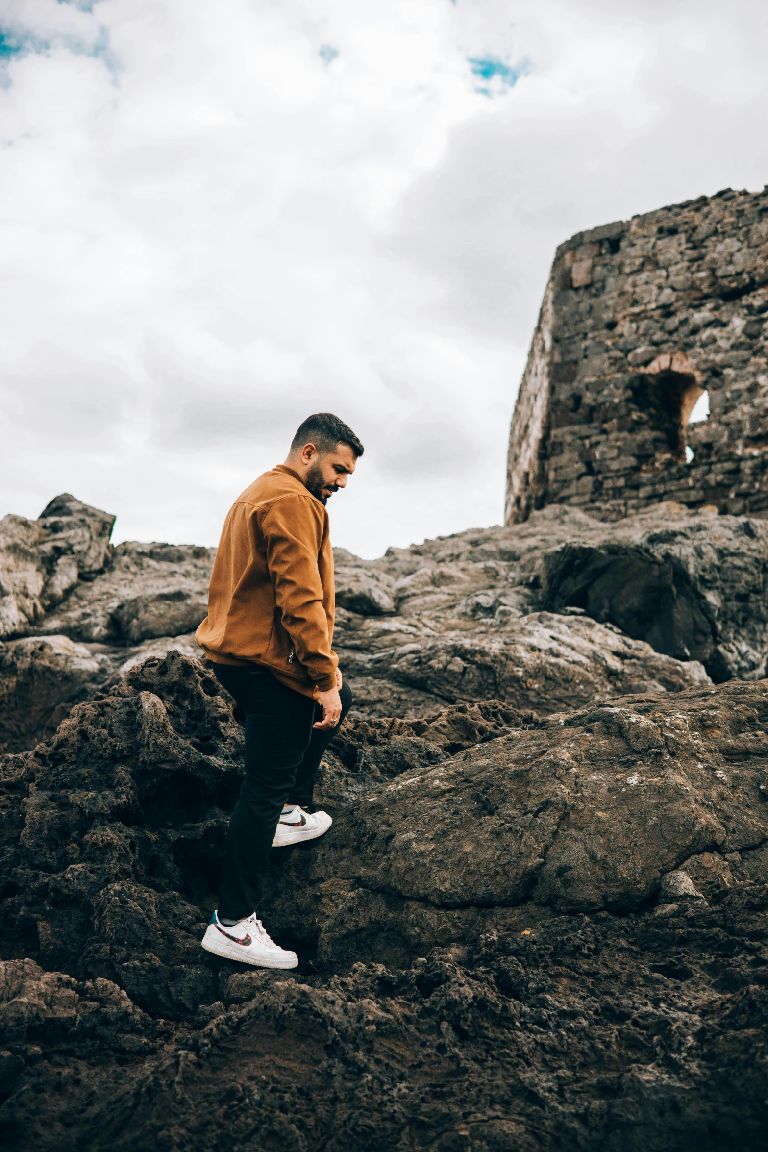 a man standing on top of a rocky hill, an album cover, pexels contest winner, happening, he is wearing a brown sweater, walking in a castle, casual streetwear, raphael lecoste