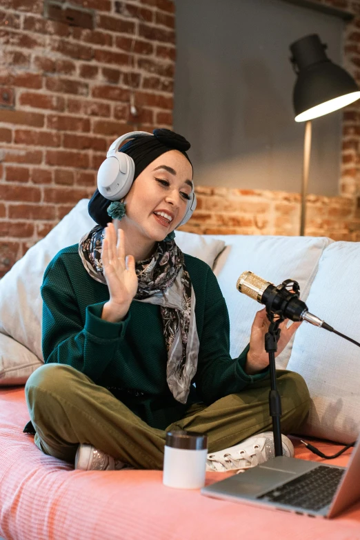 a woman sitting on top of a bed next to a laptop, an album cover, inspired by Maryam Hashemi, trending on pexels, hurufiyya, holding microphone, wearing teal beanie, asian human, talking