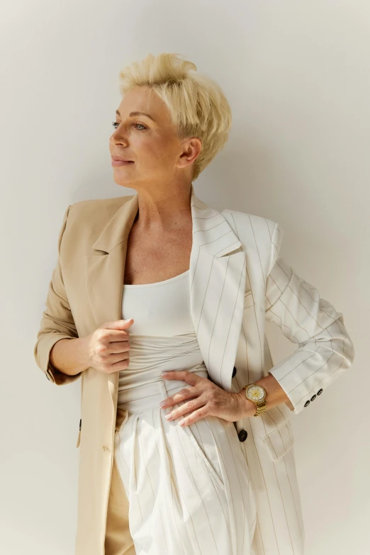 a woman standing in front of a white wall, trending on pexels, renaissance, short blond hair, business attire, giorgia meloni, celebrating