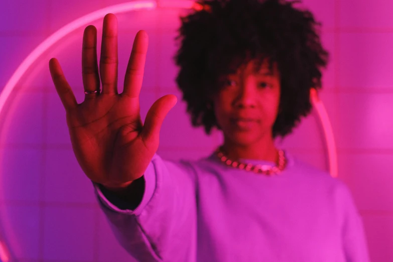 a woman making a stop sign with her hand, pexels contest winner, afrofuturism, brightly lit purple room, portrait willow smith, (night), magenta