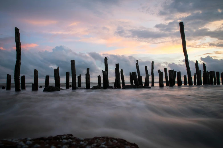 a group of wooden poles sticking out of the water, pexels contest winner, stormy setting, ruins, muted colours 8 k, slow - shutter