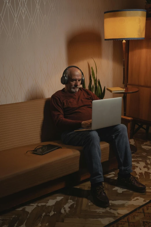 a man sitting on a couch using a laptop, by Everett Warner, pexels contest winner, headphones on head, old male, ( ( theatrical ) ), romance