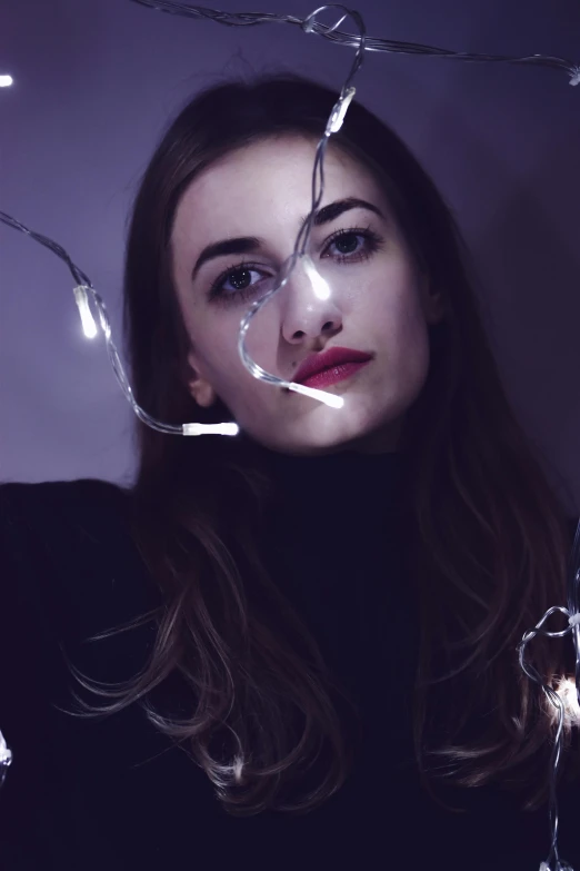a woman holding a string of lights in front of her face, an album cover, inspired by Elsa Bleda, trending on pexels, photorealism, sasha grey, disintegrating, ((portrait)), 4 k asymmetrical portrait