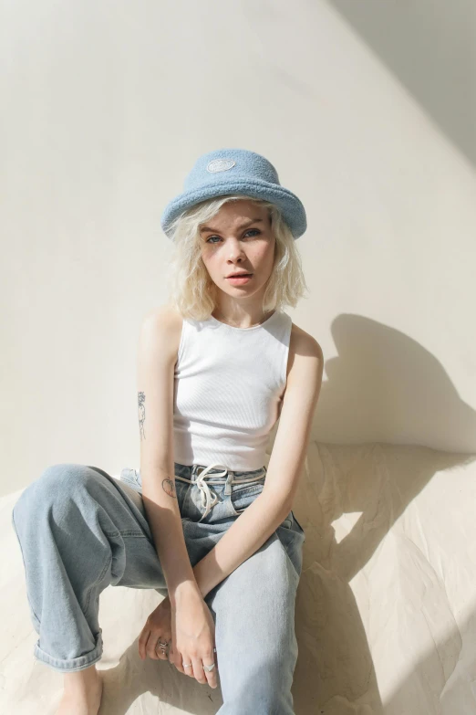 a woman sitting on a couch wearing a hat, inspired by Elsa Bleda, featured on reddit, pale blue outfit, wearing a tanktop, pale hair, uniform off - white sky