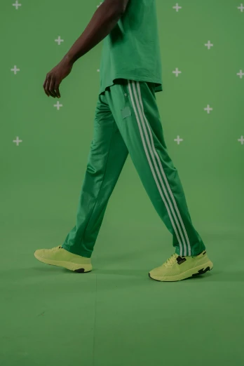 a man walking in front of a green screen, inspired by Mike Winkelmann, trending on dribble, hyperrealism, white adidas pants, on a pale background, green and yellow, stripey pants