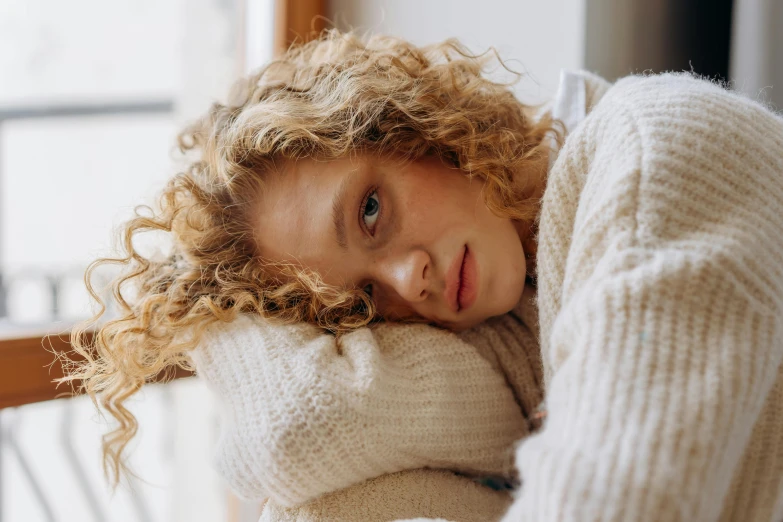 a close up of a person laying on a couch, a portrait, by Annabel Eyres, trending on pexels, curly blond hair, wearing sweater, portrait of depressed teen, portrait sophie mudd