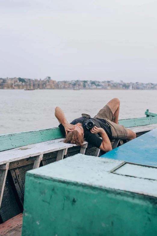 a man that is laying down on a boat, inspired by Steve McCurry, pexels contest winner, happening, holding a camera, guwahati, on an island, sleepy