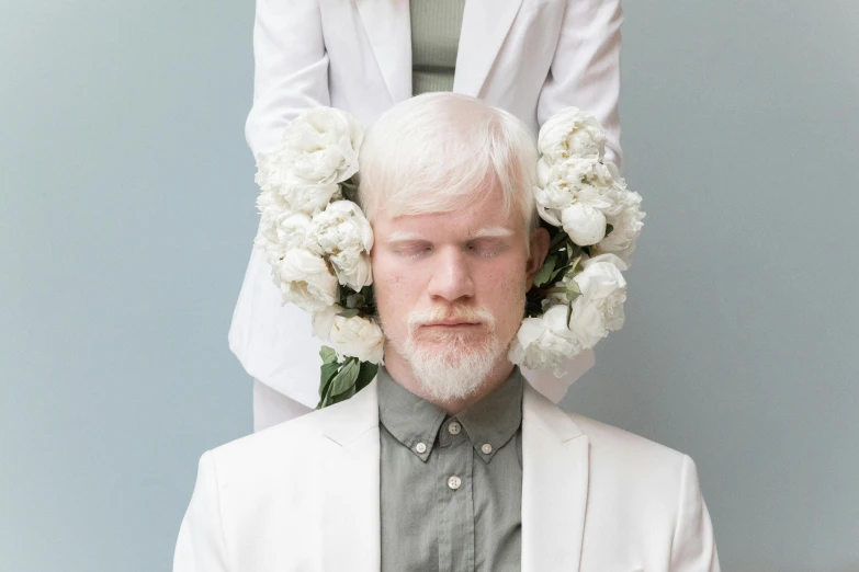 a woman standing next to a man with flowers on his head, an album cover, inspired by Dan Hillier, trending on pexels, intense albino, overalls and a white beard, wearing white suit, deux ex machina