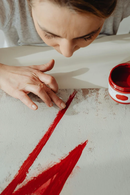 a woman is painting with red paint on a table, inspired by Lucio Fontana, trending on pexels, arbeitsrat für kunst, lacquer on canvas, handcrafted, red ink, precision