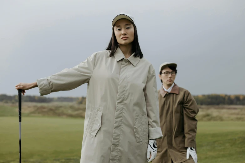 a woman standing next to a man holding a golf club, unsplash, visual art, trench coat, beige, chinese, wearing track and field suit