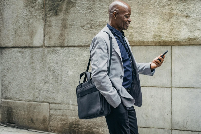 a man walking down the street looking at his cell phone, in gunmetal grey, briefcase, curated collections, well-appointed space