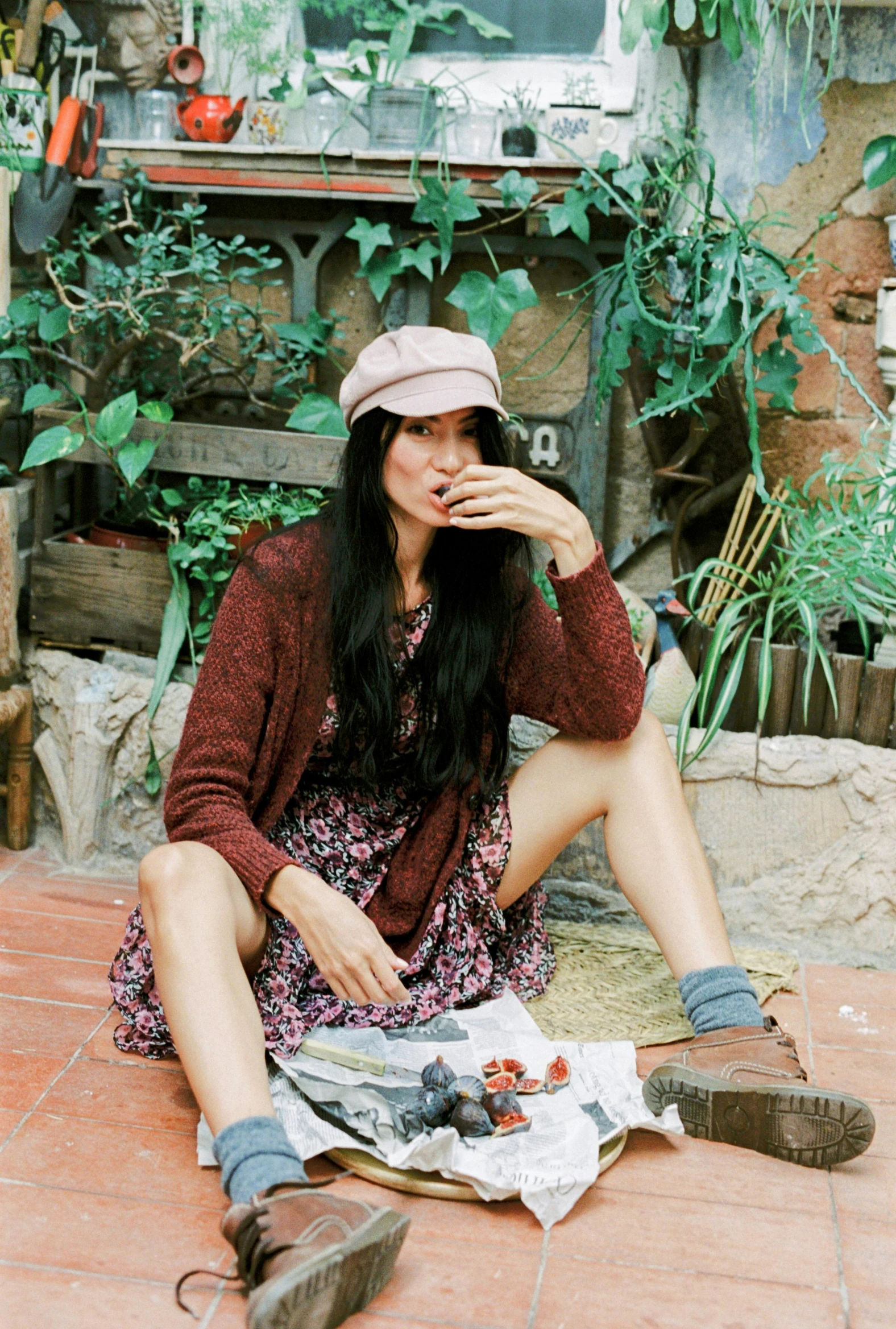 a woman sitting on the ground eating food, maroon hat, wearing a cardigan, flower child, lulu chen