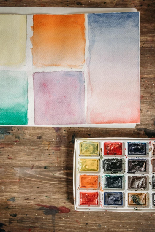 a watercolor palette sitting on top of a wooden table, inspired by artist, trending on unsplash, visual art, square shapes, ((water color)), unframed, ( watercolor )