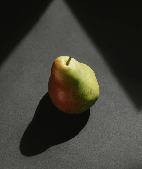 a green pear sitting on top of a black table, rectangle, half in shadow, an olive skinned, ignant