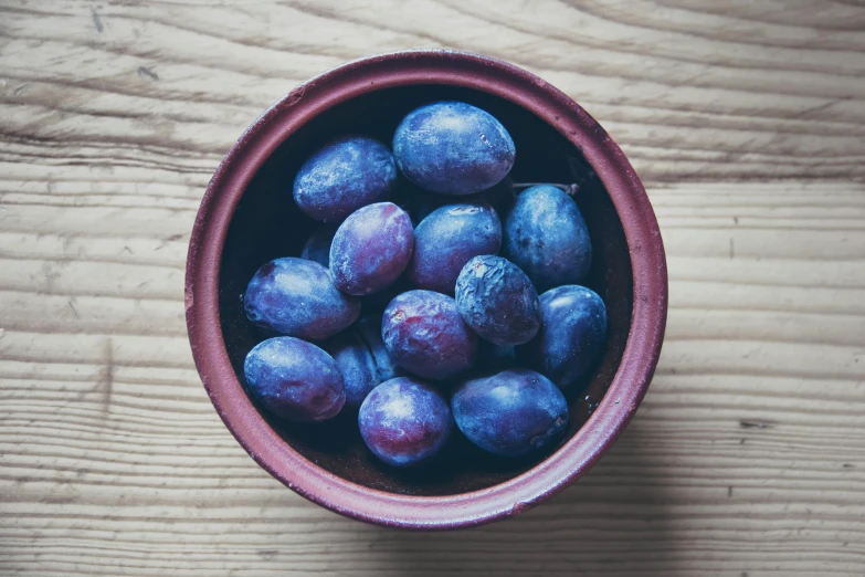 a bowl of plums on a wooden table, by Nina Hamnett, unsplash, ((purple)), grain”, round format, worn