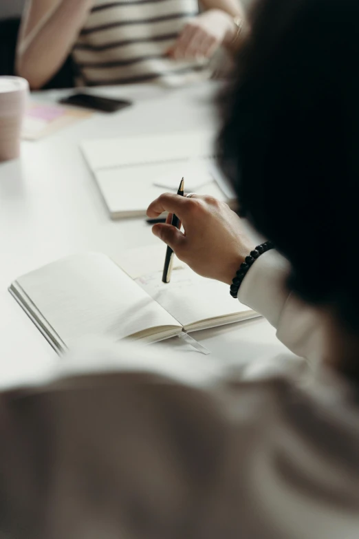 a group of people sitting around a table with notebooks, a drawing, by Robbie Trevino, pexels contest winner, black ball pen on white paper, writing a letter, close up portrait shot, instagram story