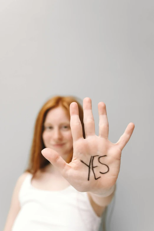 a woman holding up her hand with the word yes written on it, trending on pexels, a redheaded young woman, contracept, kek, hey buddy