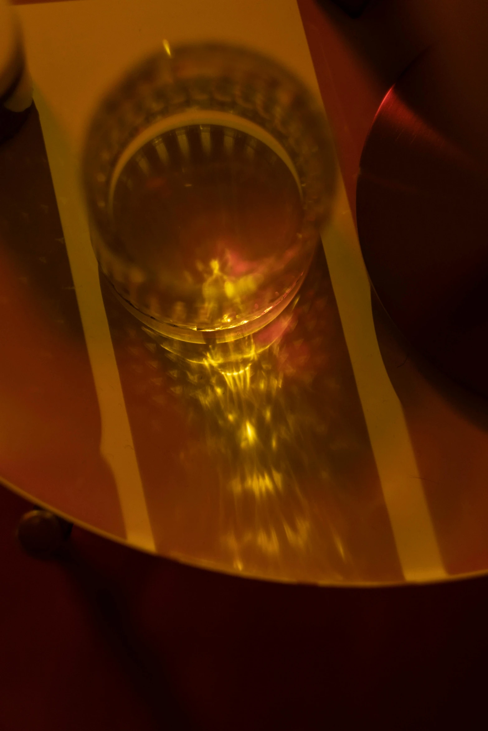 a glass of water sitting on top of a table, inspired by Otto Piene, holography, red and yellow light, detail, yellow aureole, electronics see through