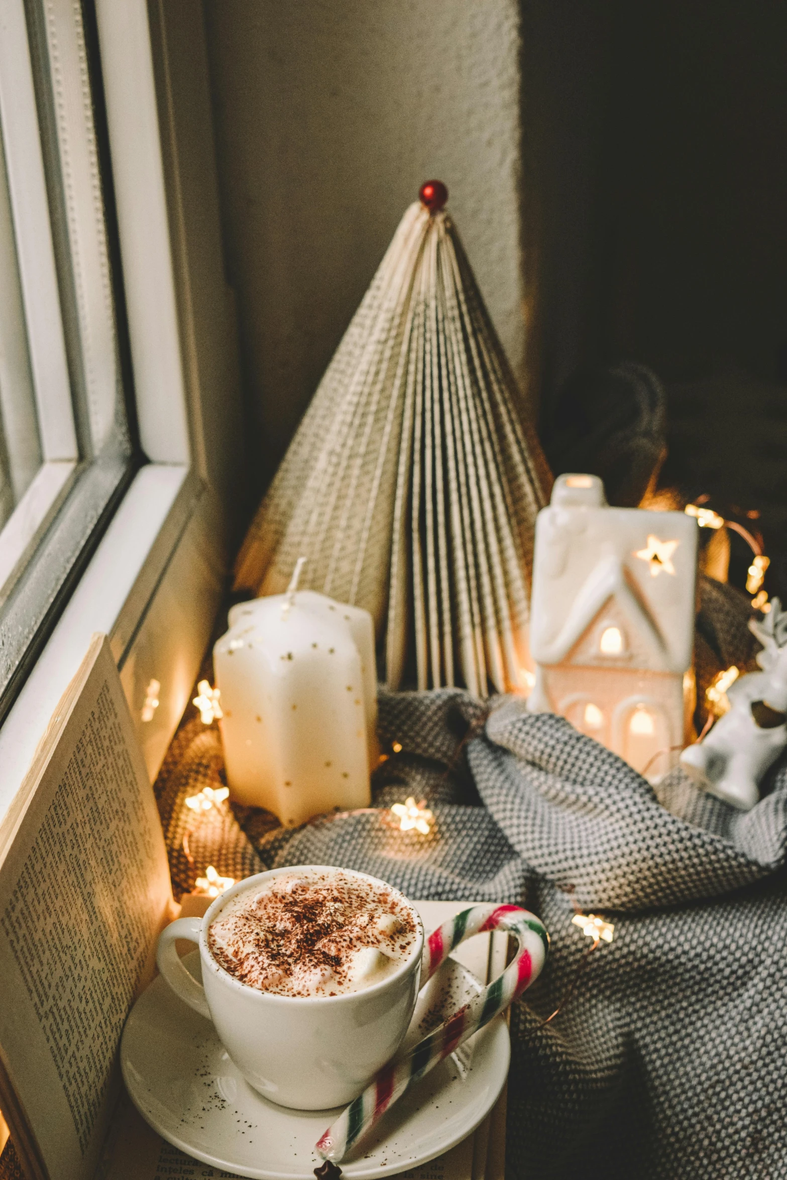 a cup of coffee sitting on top of a table next to a window, a picture, by Julia Pishtar, trending on pexels, christmas lights, reading nook, brown and cream color scheme, candy decorations