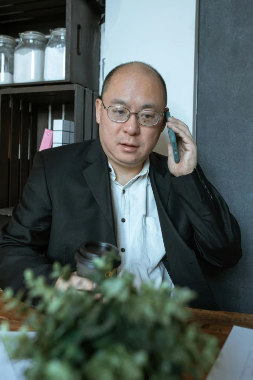 a man sitting at a table talking on a cell phone, inspired by Fei Danxu, pexels contest winner, gutai group, headshot profile picture, balding, mei-ling zhou, in the office