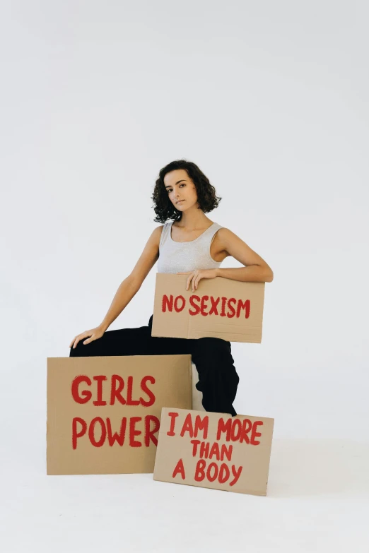 a woman holding signs that say no sexism, girls power, i am more than a boy, an album cover, by Lily Delissa Joseph, trending on pexels, feminist art, charli xcx, full body shoot, profile image, hybrid of gal gadot