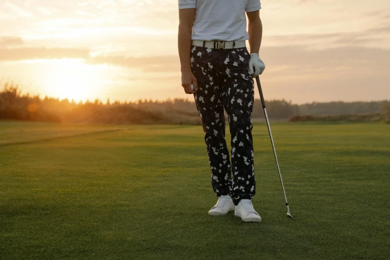 a man standing on top of a green field, clubs, wearing pants, patterned, looking off into the sunset
