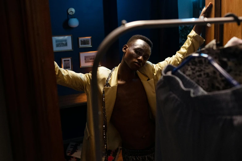 a man standing in front of a rack of clothes, an album cover, pexels, happening, adut akech, exiting from a wardrobe, behind the scenes photo, [ theatrical ]