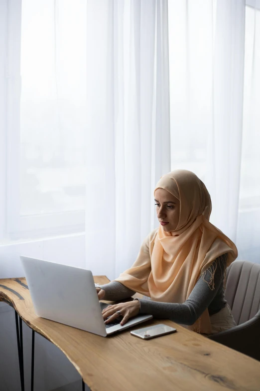 a woman sitting at a desk using a laptop computer, inspired by Maryam Hashemi, hurufiyya, tech demo, fully covered, malaysian, swedish