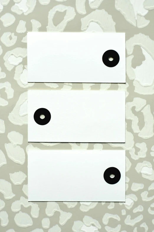 a couple of white tags sitting on top of a table, inspired by Frederick Hammersley, unsplash, suprematism, black dots, zoo, marble hole, vinyl material