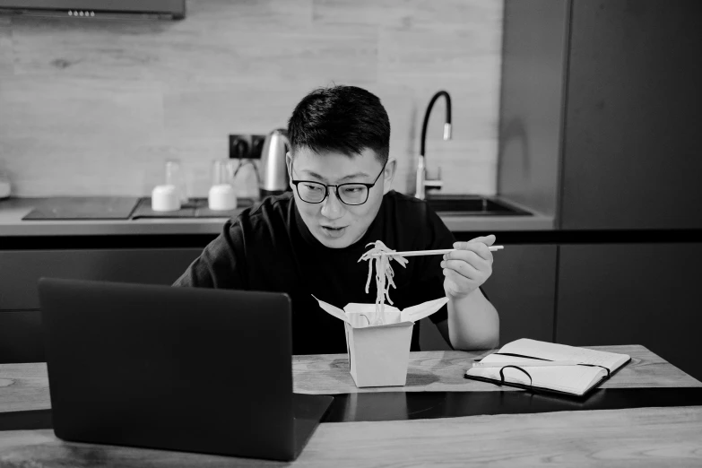 a man sitting at a table eating noodles with chopsticks, a black and white photo, inspired by Fei Danxu, pexels contest winner, sitting in front of computer, wearing black frame glasses, gif, product introduction photo