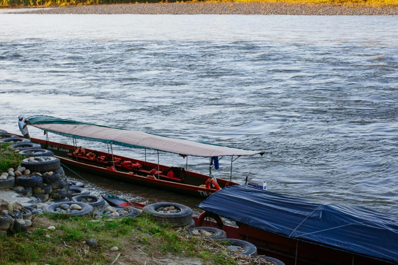 a boat sitting on top of a river next to a lush green hillside, inspired by Steve McCurry, pexels contest winner, sumatraism, small canoes, grey, gold, lit from the side