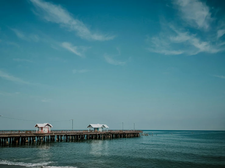 a pier sitting on top of a beach next to the ocean, pexels contest winner, light blue clear sky, background image, fishing town, moody : : wes anderson