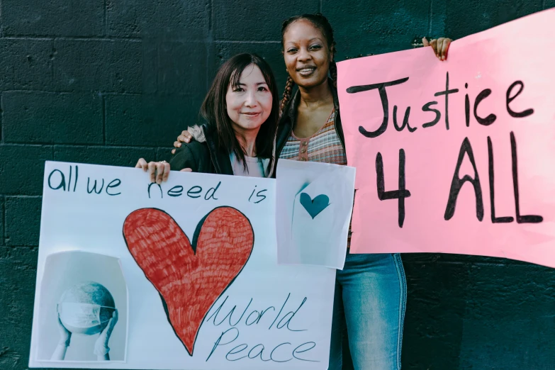 a couple of women standing next to each other holding signs, a photo, by Julia Pishtar, trending on unsplash, black arts movement, world peace, ayami kojima and lyde caldwell, a friend in need, -n 4