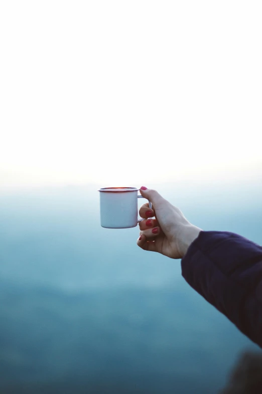 a person holding a cup of coffee on top of a mountain, minimalism, gazing off into the horizon, no text, awkwardly holding red solo cup, blur dreamy outdoor