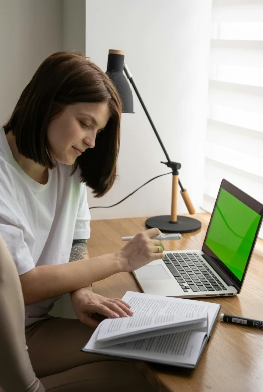 a woman sitting at a desk working on a laptop, green and white, textbooks and books, taken in 2022, promo image