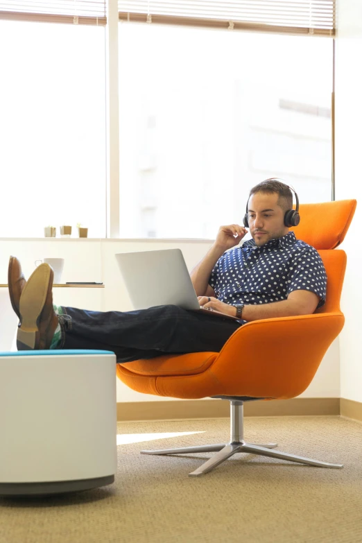 a man sitting in a chair with a laptop on his lap, floating headsets, cubical meeting room office, orange hue, curated collections