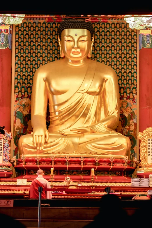 a person standing in front of a golden buddha statue, a statue, sitting down, wearing red robes, statues