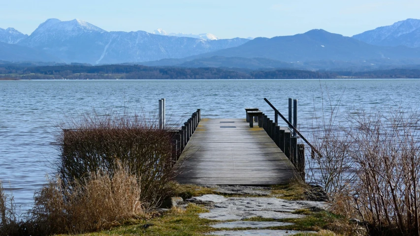 a dock next to a body of water with mountains in the background, by Niko Henrichon, pexels contest winner, visual art, walkway, distance view, the alps are in the background, where a large