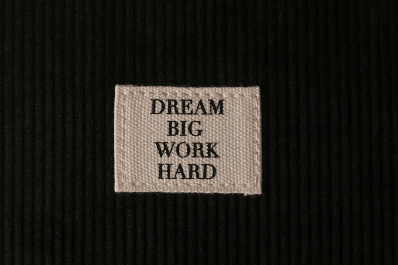 a label that says dream big work hard, by Abraham van Beijeren, realism, off-white, black, panel, threads