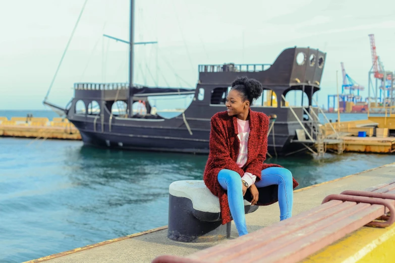 a woman sitting on a bench in front of a boat, pexels contest winner, brown skin, pirate clothing, aida muluneh, harbour