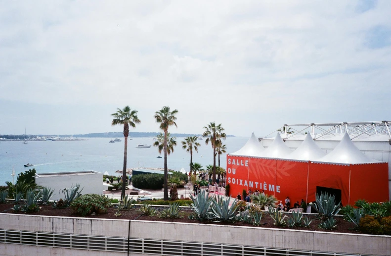 a red building sitting next to a body of water, by Nathalie Rattner, pexels contest winner, fauvism, cannes, basquiat, view of the ocean, sofia coppola
