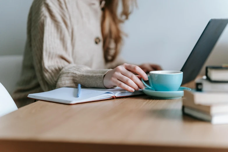 a woman sitting at a table with a laptop and a cup of coffee, trending on pexels, avatar image, writing a letter, background image, student