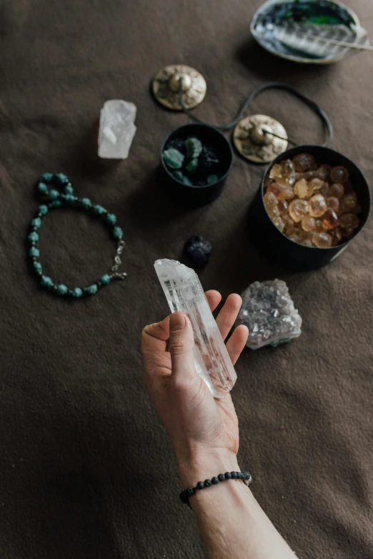 a person holding a crystal on top of a table, a still life, trending on pexels, runic symbols, flat lay, handheld, white