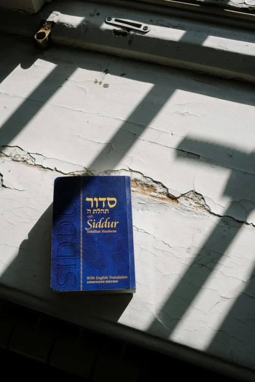 a blue book sitting on top of a window sill, by Douglas Shuler, trending on reddit, hebrew, sun flare, as well as scratches, religion