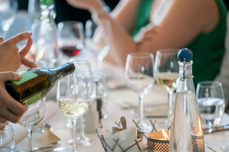 a group of people sitting at a table with wine glasses, upclose, white wine bottle, multiple stories, amanda lilleston