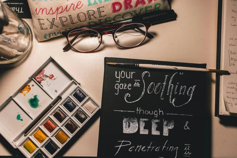 a blackboard sitting on top of a desk next to a pair of glasses, a photorealistic painting, trending on pexels, calligraphic poetry, deep colour\'s, flatlay, art set