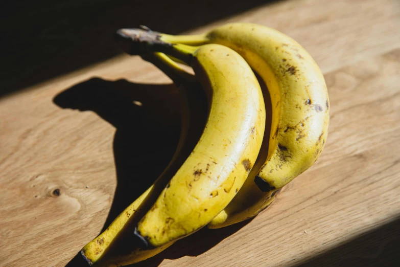 a couple of bananas sitting on top of a wooden table, in the sun, listing image, thumbnail, high quality product image”