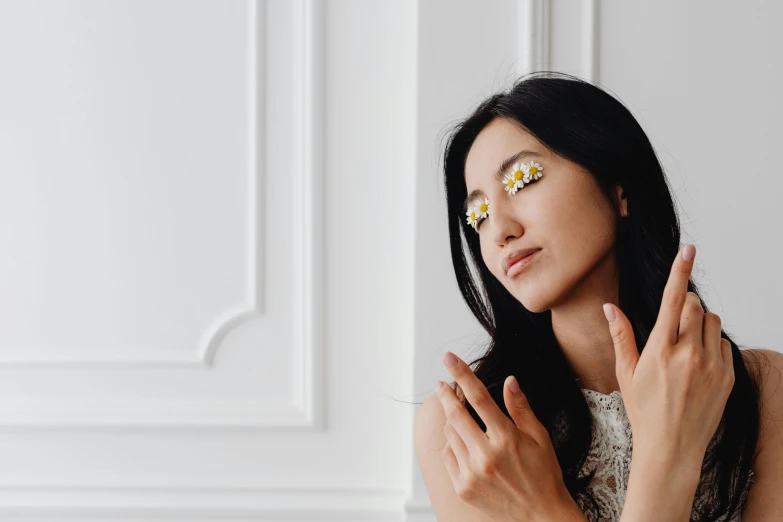 a woman standing in front of a white wall, inspired by Ruth Jên, trending on pexels, gold flowers, mirror eye implants, offering the viewer a pill, chamomile